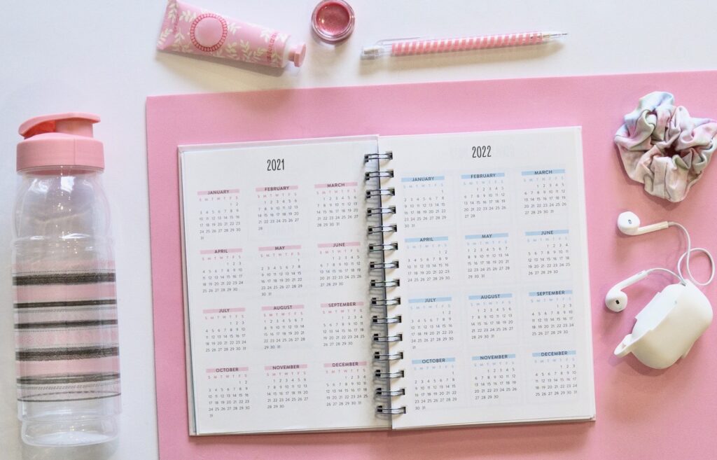 Overhead view of a feminine calendar flatlay on a pink background