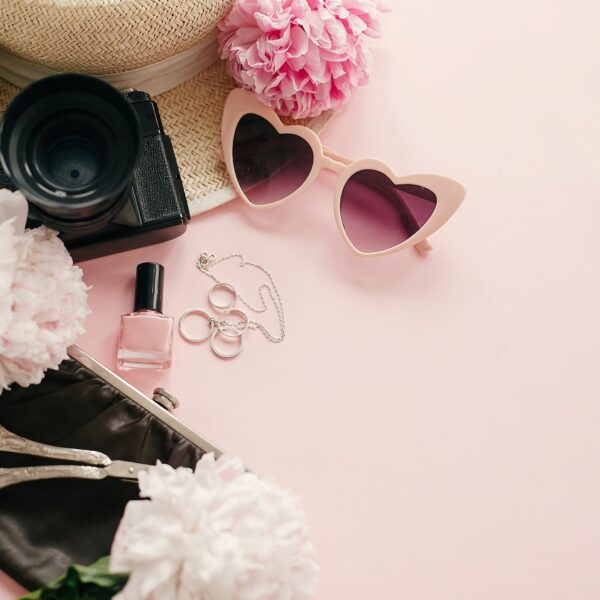 Stylish girly flat lay with pink peonies, photo camera, retro sunglasses, jewelry